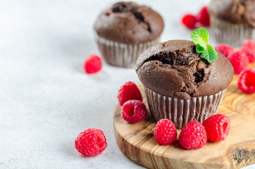 Three chocolate muffins on a wooden board with fresh raspberries, copy space for your text