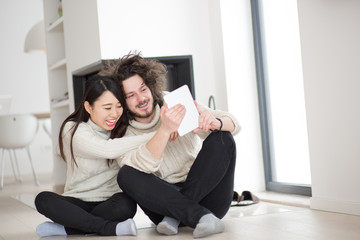 multiethnic couple using tablet computer in front of fireplace