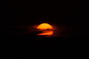 Big orange sun in clouds at sunset on black background.