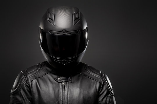 Man wearing a black leather motorcycle jacket and helmet on dark background.