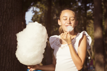 Girl eating cotton candy in a summer park  - obrazy, fototapety, plakaty