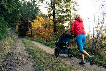 Running mother with stroller enjoying motherhood at autumn sunset