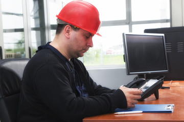 Engineer with red helmet typing the message  in the power plant control center