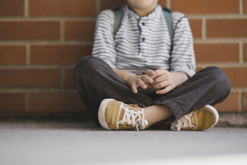 A little boy sitting cross legged in front of a brick wall wearing yellow sneakers
