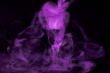 Smoke into cocktail glass on a black background. Witch potion background for Halloween. Unusual bar drink.