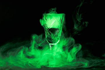 Smoke into cocktail glass on a black background. Witch potion background for Halloween. Unusual bar drink.