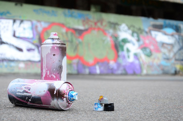 Several used spray cans with pink and white paint and caps for spraying paint under pressure is...