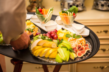 Waiter carrying tray with plates with fruits and vegetables on some festive event