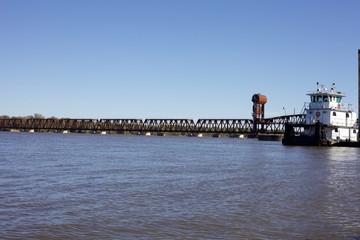 Tug boat travels northbound beyond a train bridge on the mississippi river outside bulington iowa