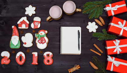 Top view of blank notebook on wooden background with xmas decorations, copy space. Christmas background with empty notebook, gingerbread cookies and hot cocoa, red gift boxes. Flat lay