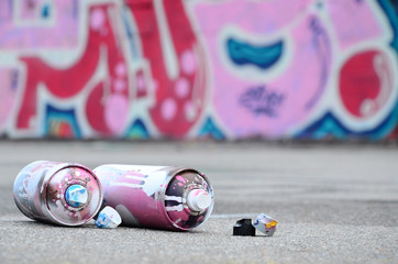 Several used spray cans with pink and white paint and caps for spraying paint under pressure is...