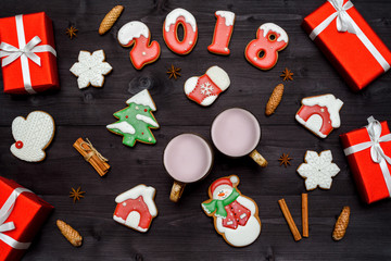 Fototapeta na wymiar Christmas background with red gift boxes, happy new year 2018 sign symbol, gingerbread cookies (santa, snowman, snowflake) and two cups of cocoa, cinnamon sticks and star anise. Flat lay, top view