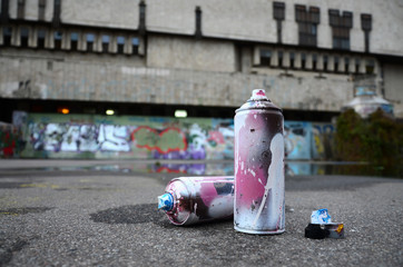 Several used spray cans with pink and white paint and caps for spraying paint under pressure is...