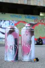 Several used spray cans with pink and white paint and caps for spraying paint under pressure is...