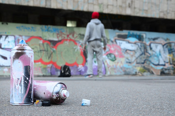 Several used spray cans with pink and white paint lie on the asphalt against the standing guy in...