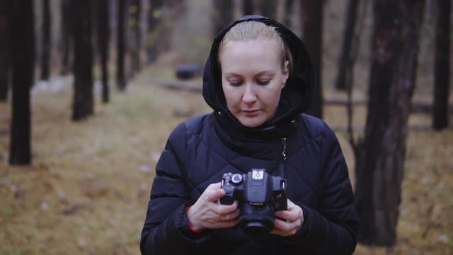 a professional photographer walks through the forest with a camera in his hands and looks at the pictures she took. autumn forest, photography of landscapes. cinematic shot, slow motion.