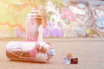 Several used spray cans with pink and white paint and caps for spraying paint under pressure is...