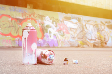 Several used spray cans with pink and white paint and caps for spraying paint under pressure is...