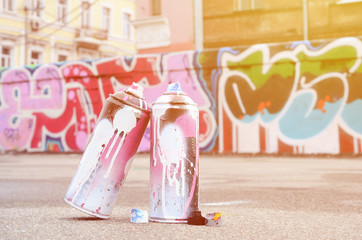 Several used spray cans with pink and white paint and caps for spraying paint under pressure is...