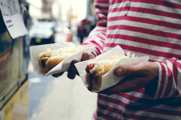 Someone holding two hotdogs in the street