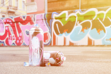 Several used spray cans with pink and white paint and caps for spraying paint under pressure is...