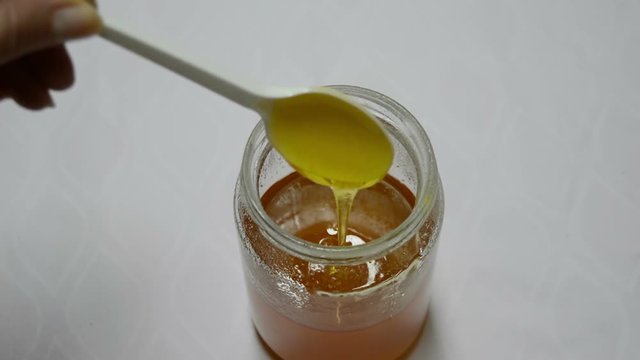 Quality Honey Pouring a Continuous Stream / Close-up bottle of honey on a white background isolated, spoon of continuous stream of honey