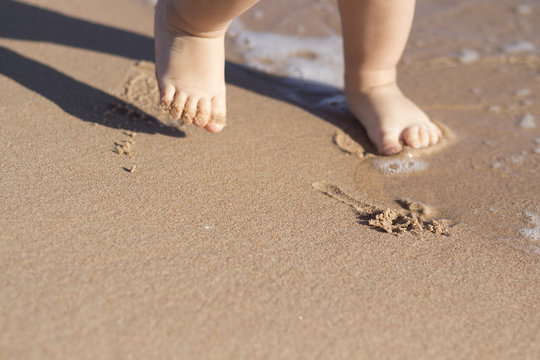 Legs of children stand on the beach. Baby feet in the sand. Summer beach background. Summertime holidays concept. Copy space.