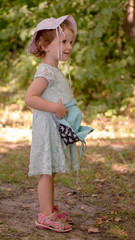 Portret małej  słodkiej dziewczynki w parku, rozmyte tło, cała postać.