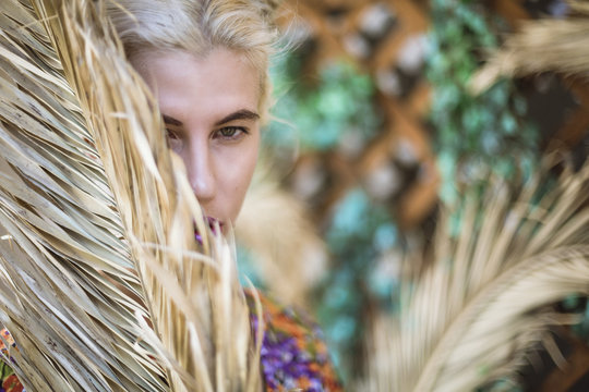 blond girl hiding behind dry palm frond