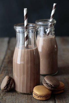 Bottles of chocolate milk with straws and macaroons on wooden table
