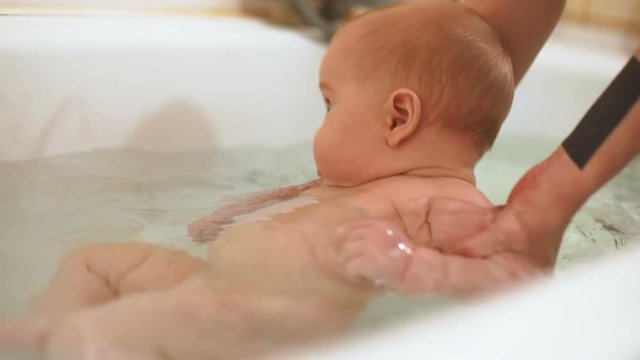 little kid bathing mother hands support clean body skin care healthy concept babyboy washing taking bath water tub home beauty human parenting glad infant adorable child calm interested newborn fun