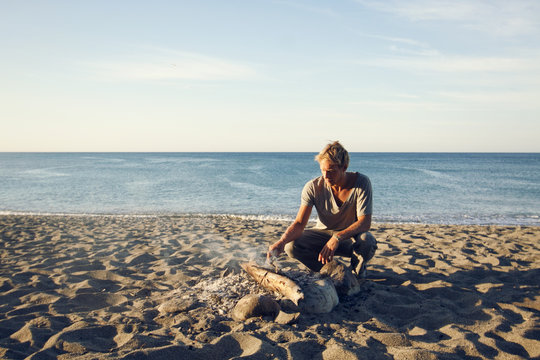 Young man on the beach making a bonfire