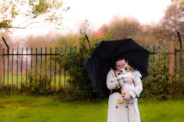 Szczeniak Jack Russell terrier na rękach swojej właścicielki. Zdjęcie w plenerze w wietrzny deszczowy jesienny dzień. - obrazy, fototapety, plakaty