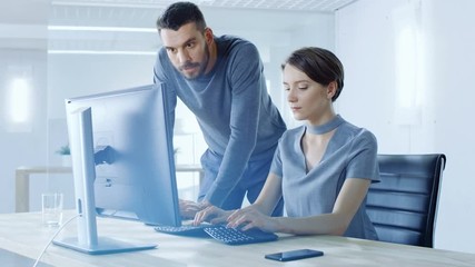 Male and Female Office Workers Discussing Information Shown on Personal Computer. Office is Modern and Bright. Shot on RED EPIC-W 8K Helium Cinema Camera.