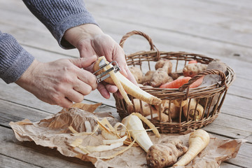 Male hands peeling some parsnips next to a basket filled with root vegetables
