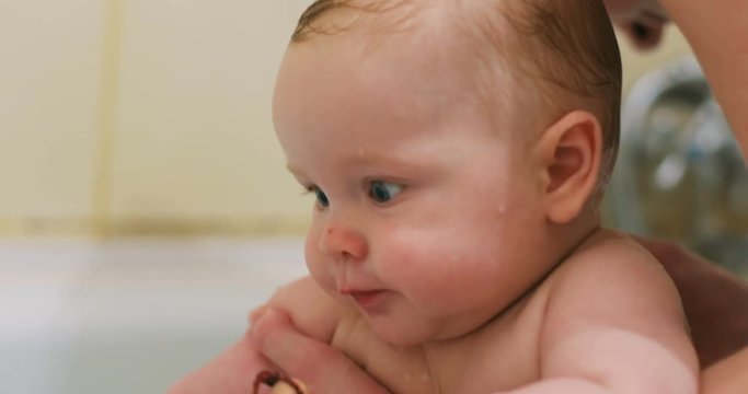 closeup portrait baby bou sitting bath bathing mother hands caressing wet hair head healthy body little child chubby cheeks big surprised eyes looking camera gnawing toy teethers funny happy toddler
