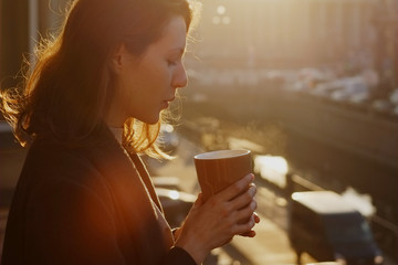 Woman blowing on hot coffee at the sunset