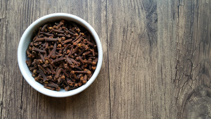 Cloves in white glass bowl on wooden background