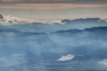 Elevated view through glowing autumn mist and sunbeams to Lake Bled, Bohinj mountain range and Pokljuka plateau Julian Alps Triglav National Park from Stol Karavanke Carniola Gorenjska Slovenia Europe