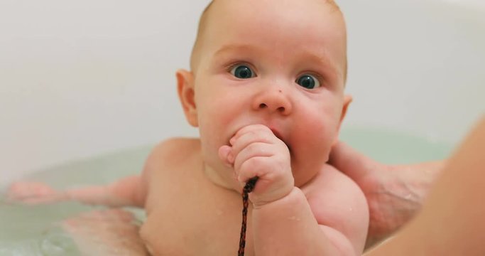 Baby boy bathing bathtub hands splashing water fun gnawing toy teethers babies funny toddler portrait sweet cute child six months old bath mother hands plump little infant chubby cheeks natural beauty