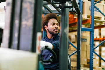 Young male worker driving a forklift in a warehouse.