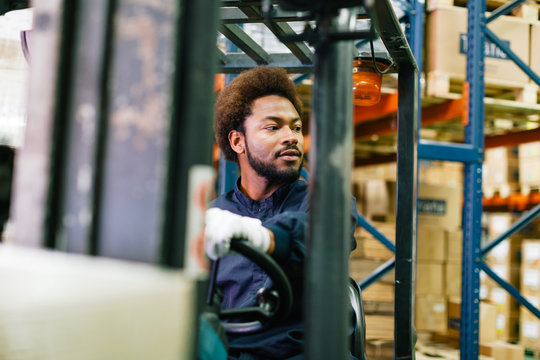 Young male worker driving a forklift in a warehouse.