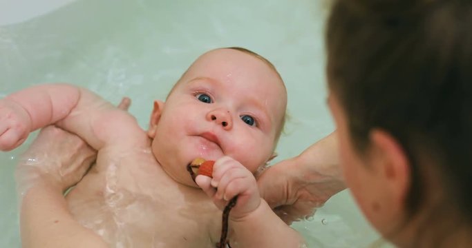 sweet baby boy swimming lie back water bathing bathtub gnawing teething toy teethers cute child splashing mother hands holding strong naked body son healthcare gentle skin carefree childhood enjoying