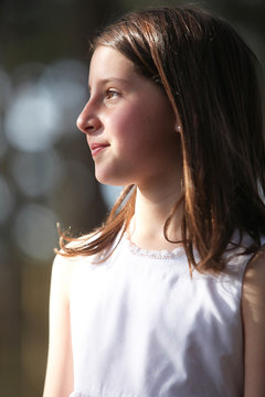 Side profile of young  girl wearing white dress in bright outdoor sunlight