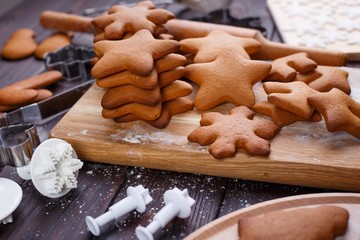 Freshly baked ready to decorating gingerbread cookies with cutters and baking utensils on the table, close up. Traditional festive sweets, Christmas food preparing