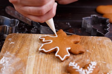 Confectioner decorating gingerbread cookies with confectionery icing, close up. Traditional Christmas sweets, festive food making