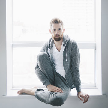 Man In A Grey Hoodie And Sweat Pants Sits At A Window