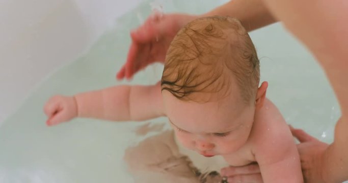 curious interested baby boy taking bath playing water splash hands toys mother hands caress head gentle loving touch mom child cute calm beautiful toddler innocence game fun joy hapiness parenting