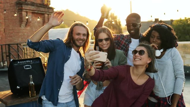 Young friends making funny selfies at the rooftop party in sunset. The brick wall background. Urban space. Outdoor. Multi-etnic