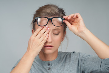 Tired woman in eyeglasses, covering eyes with hands